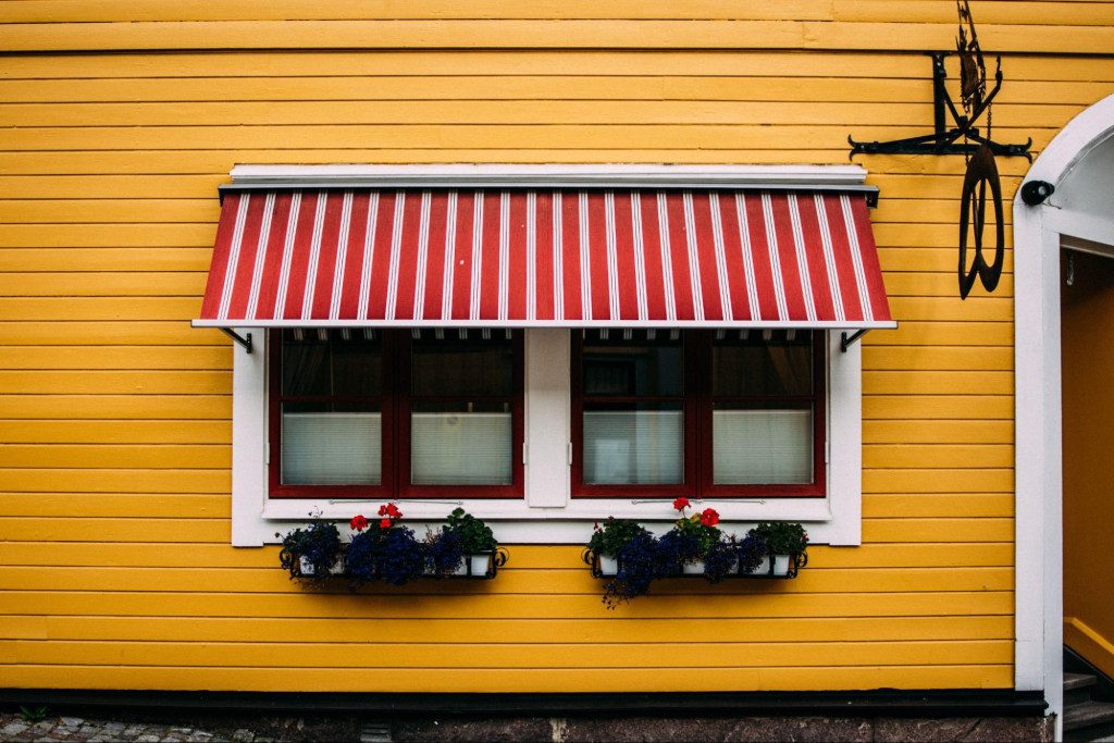 A red and white striped stationary awning in contrast with a yellow outside wall of a house