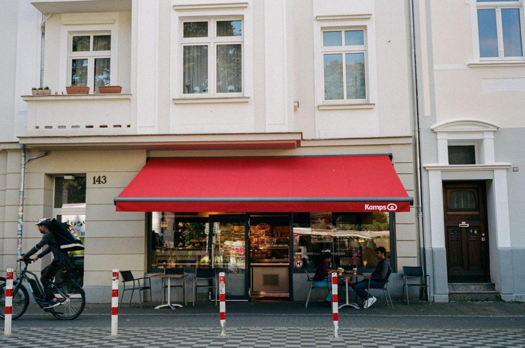 Red outdoor retractable awning installed over a seating area of a street coffee shop